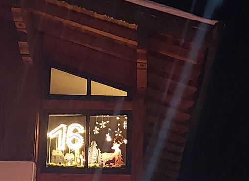 Ein festlich dekoriertes Fenster mit der Zahl 16 und einem Reh. Umgeben von schneeweißen Schneeflocken und Sternen.