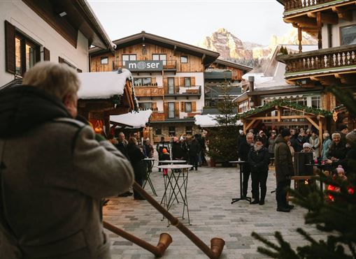 Eine winterliche Veranstaltung in einem malerischen Dorf. Menschen versammeln sich im Freien vor traditionellen alpinen Gebäuden.