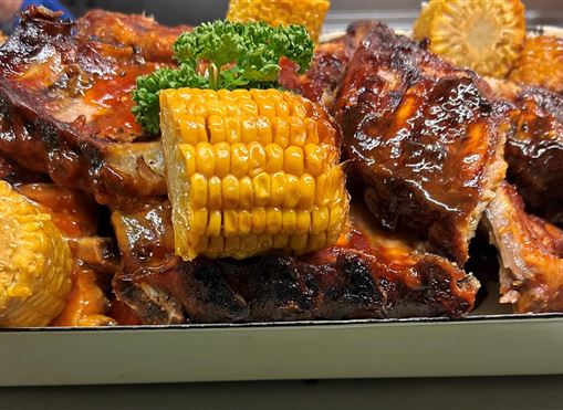 A delicious plate of grilled ribs and corn on the cob, garnished with parsley. The ribs are shiny and well-glazed.