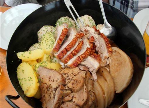 Ein herzhaftes Gericht mit zartem Fleisch, Beilagen aus Kartoffeln und Gemüse. Es wird in einer großen Schale serviert und garnierte mit Kräutern.