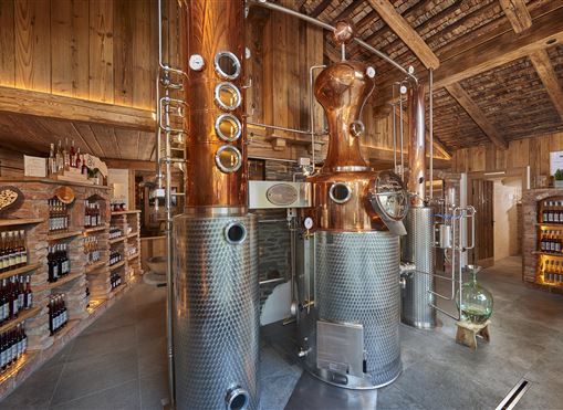 Eine moderne Brennerei mit glänzenden Kupfer- und Edelstahltanks. Regale mit Flaschen sind im Hintergrund sichtbar.