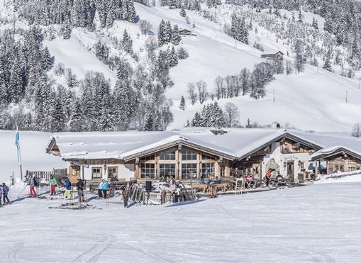 Eine elegante Berghütte im Schnee, umgeben von schneebedeckten Bäumen. Skifahrer genießen die winterliche Landschaft und die frische Luft.