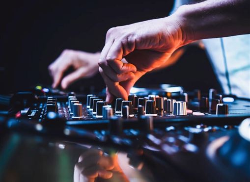 Ein DJ mixet Musik an einem Mischpult mit verschiedenen Reglern. Die Atmosphäre ist energiegeladen und kreativ.