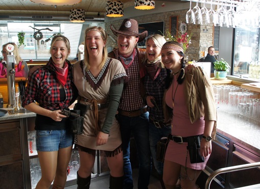 Eine Gruppe von fünf fröhlichen Menschen in Westernkleidung lächelt in einer Bar. Die Atmosphäre ist lebhaft und einladend.