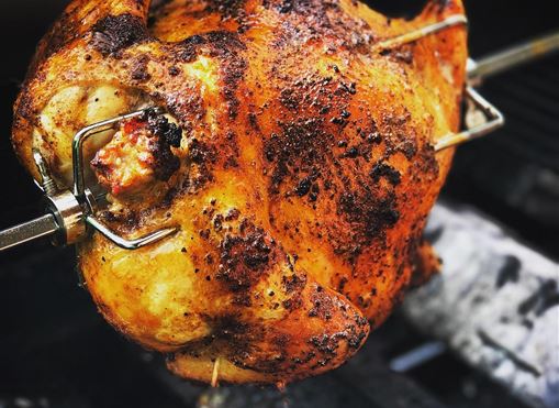 Ein gut gegrilltes Hähnchen am Spieß, perfekt knusprig und goldbraun. Es liegt auf einem Grill mit glühenden Kohlen.