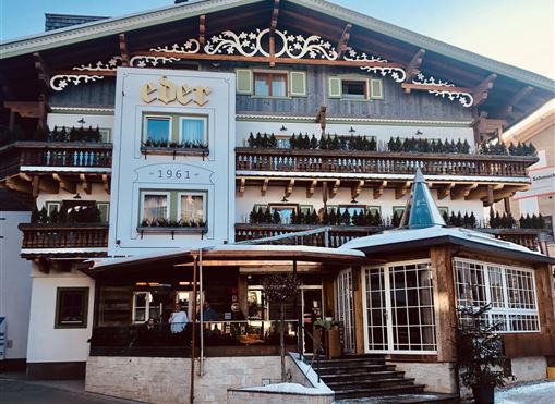 Ein traditionelles Alpenhotel mit einem schönen Holzgebäude und verzierten Balkonen. Es liegt in einer schneebedeckten Umgebung und strahlt Gemütlichkeit aus.