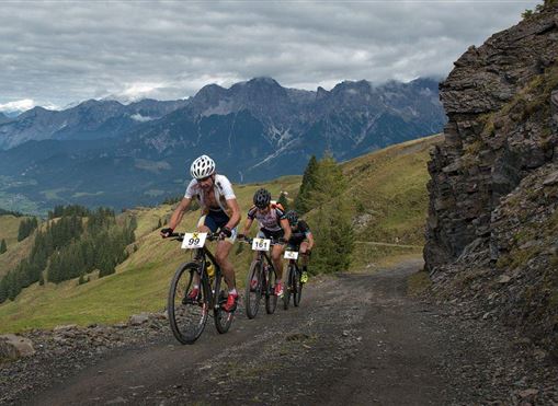 Cyclist on a dirt road in the mountains. In the background, impressive mountains and a cloudy sky can be seen.