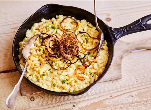Ein köstliches Gericht in einer gusseisernen Pfanne, serviert mit knusprigen Zwiebelringen. Das Essen besteht aus cremiger Pasta und grünen Zwiebeln.
