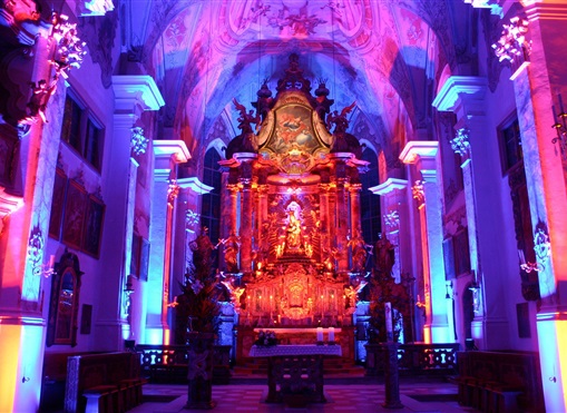 Ein wunderschöner Kircheninnenraum mit bunten Lichtern. Der Altar ist reich verziert und strahlt in warmen Farben.