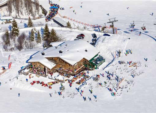 A ski hut surrounded by snow, with many people having fun. Skiers are using the slopes and enjoying the winter landscape.