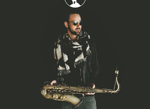 Ein Musiker hält ein Saxophon und trägt eine Sonnenbrille sowie einen Schal. Der Hintergrund ist dunkel, und der Schriftzug "MAX THE SAX" ist sichtbar.