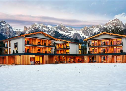 Ein modernes Gebäude aus Holz vor einer malerischen Berglandschaft. Der Schnee rundherum sorgt für eine gemütliche Winteratmosphäre.