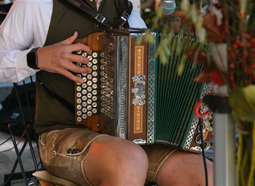 Ein Musiker spielt Akkordeon in traditioneller Tracht. Im Hintergrund sind florale Dekorationen zu sehen.