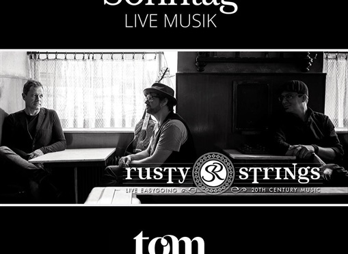 Eine Schwarz-Weiß-Aufnahme von drei Musikern, die in einem gemütlichen Raum sitzen. Sie spielen Live-Musik unter dem Namen "Rusty Strings".