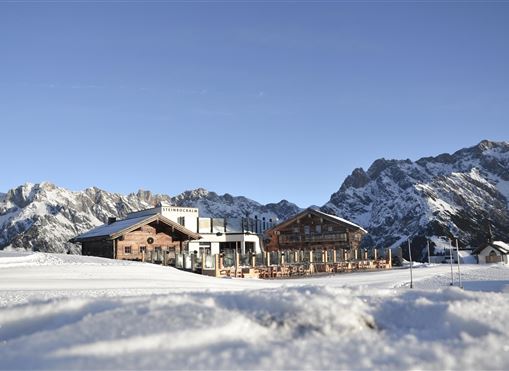 Ein charmantes Berghaus in der verschneiten Landschaft. Im Hintergrund erheben sich majestätische Berge unter einem klaren Himmel.