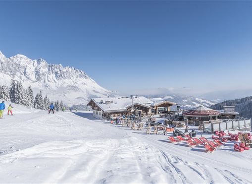 Ein malerischer Winterort mit schneebedeckten Bergen und einem gemütlichen Restaurant. Skifahrer genießen die Pisten in der nahegelegenen Schneeidylle.