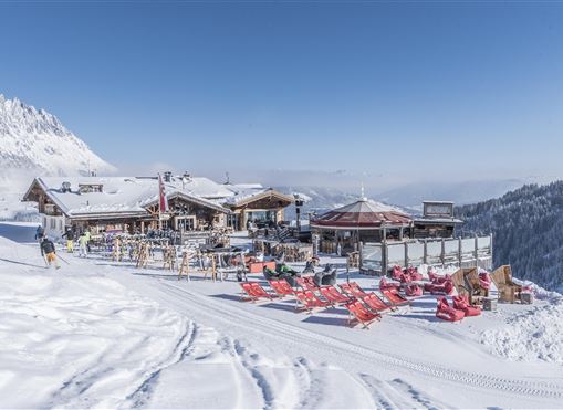 Eine gemütliche Alpenhütte inmitten einer schneebedeckten Landschaft. Rote Liegestühle laden zum Entspannen in der Sonne ein.