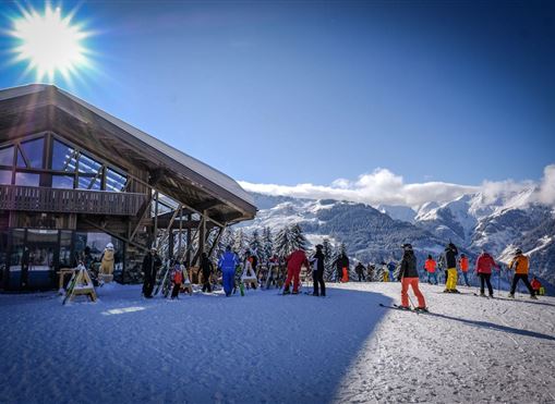Eine Skihütte umgeben von schneebedeckten Bergen. Skifahrer und Snowboarder genießen den sonnigen Tag im Schnee.