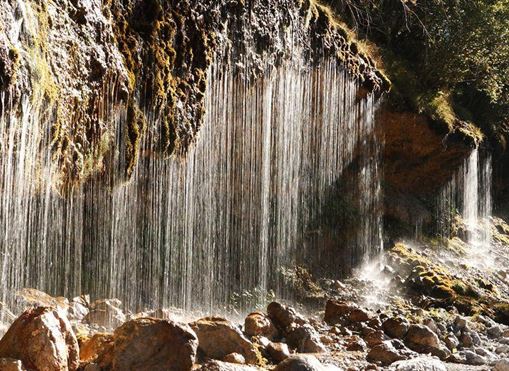 Ein Wasserfall fließt sanft über steinige Felsen. Das Licht sorgt für glitzernde Effekte im Wasser.