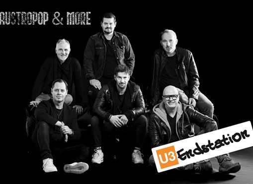 Sechs Musiker posieren in einer schwarzen Umgebung. Im Vordergrund ist ein großes Schild mit der Aufschrift "U3 Endstation" zu sehen.