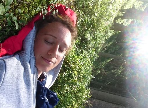 Eine Person liegt entspannt im Gras, umgeben von Pflanzen. Die Sonne scheint hell und sorgt für eine angenehme Atmosphäre.