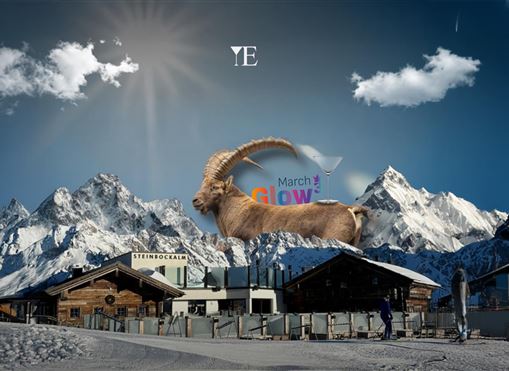 A majestic goat symbol stands in front of an impressive mountain landscape. The sky is clear with few clouds, and the scene radiates a wintery tranquility.