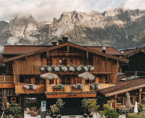 Ein rustikales Holzhaus mit Blumenschmuck, umgeben von beeindruckenden Bergen. Die Atmosphäre ist gemütlich und einladend.