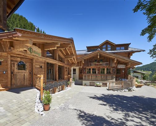 Ein charmantes, hölzernes Gebäude in einer gebirgigen Umgebung. Der klare Himmel und die grünen Bäume verleihen der Szene eine einladende Atmosphäre.